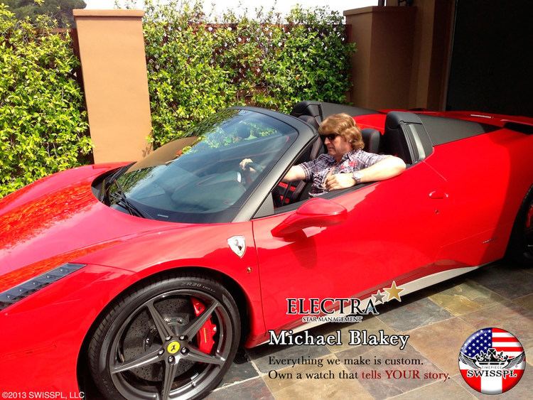 Michael Blakey riding his Red 458 Spider Sports Car while wearing a purple checkered shirt and sunglasses.
