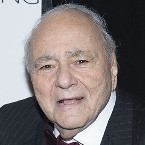 Michael Constantine smiling, with white hair, wearing a black striped coat over white long sleeves, and a black bow tie.