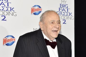 Michael Constantine with a big smile on his face, wearing a black striped coat over white long sleeves, and a black bow tie.