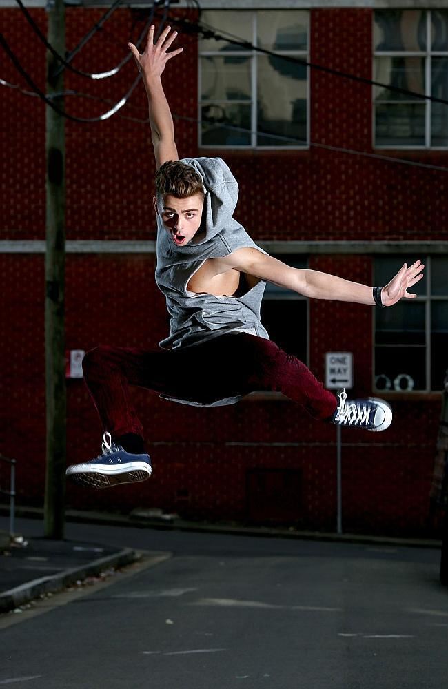 Michael Dameski jumping while wearing a gray hooded sando, maroon pants, and black and white sneakers