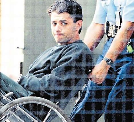 Michael Kanaan in his wheelchair wearing black sweatshirt accompanied by policemen