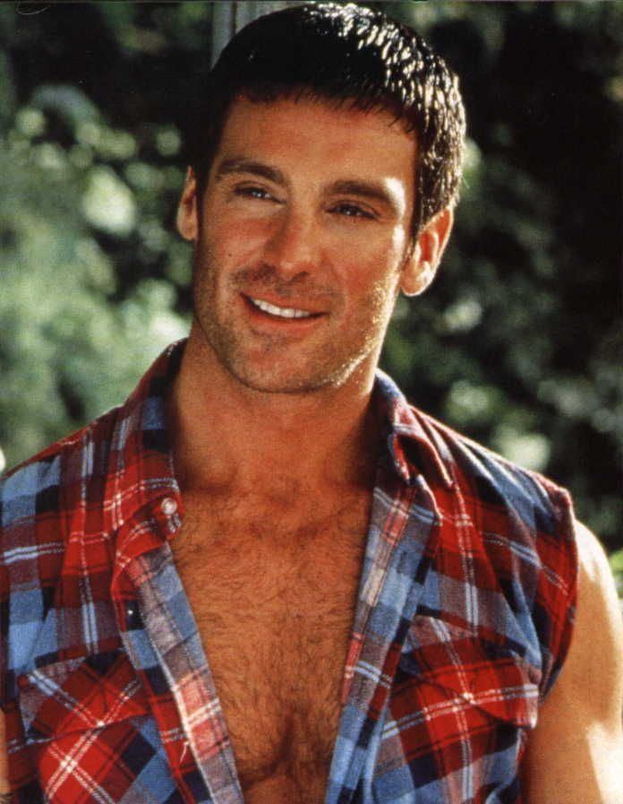 Michael T. Weiss with short hair & smiling while wearing a checkered red and blue polo shirt