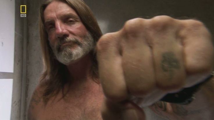 Michael Thompson with long hair and showing his fist with a tattoo.