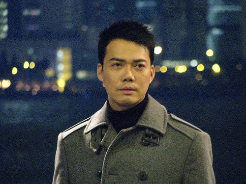 Michael Tse looking at something while wearing a gray trench coat and black turtle-neck inner shirt