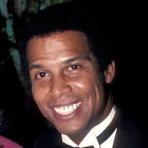 Michael Warren smiling and wearing a black coat, white long sleeves, and bow tie