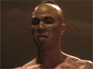 Michel Qissi as Tong Po with a furious face, topless, with a tattoo on his body in a movie scene from Kickboxer, a 1989 American martial arts film.
