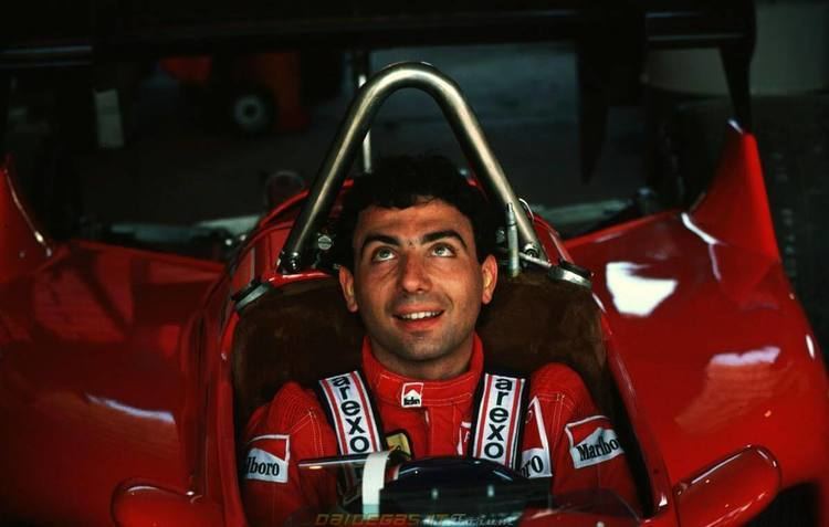 Michele Alboreto smiling while driving a red car and wearing a red and white racing suit