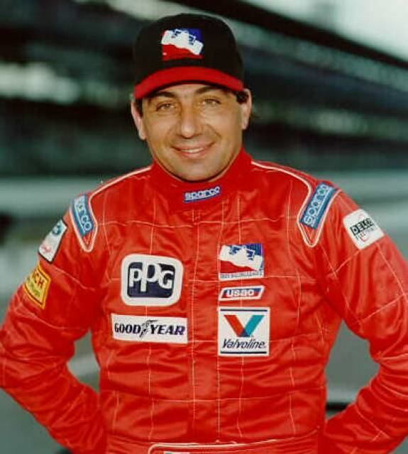 Michele Alboreto smiling while wearing a red racing suit and black and red cap