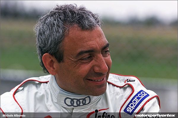Michele Alboreto smiling while wearing a white and red racing suits
