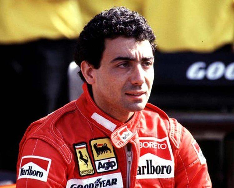 Michele Alboreto with a tight-lipped smile while looking afar and wearing a red racing suit