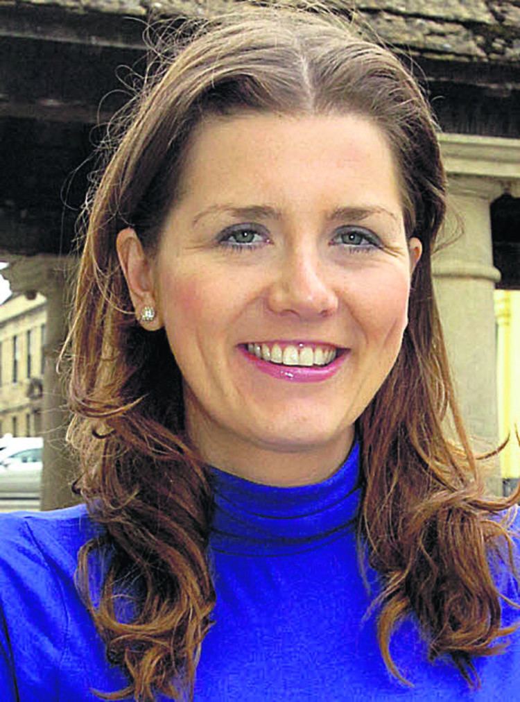 Michelle Donelan smiling while wearing a blue blouse and earrings