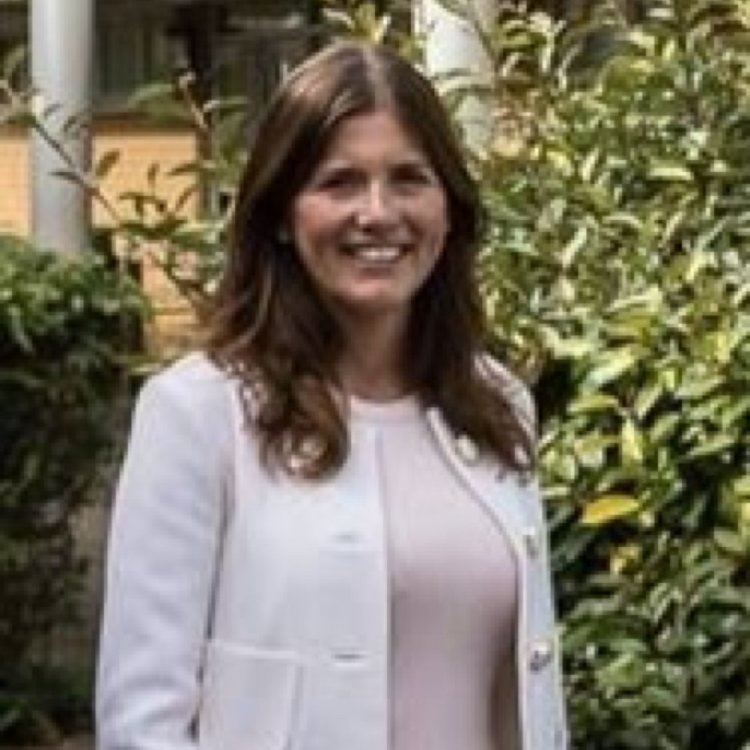 Michelle Donelan smiling while wearing a white coat and light pink blouse