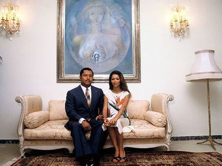 Jean-Claude Duvalier sitting on a couch with his wife Michele Bennett who is wearing white floral dress
