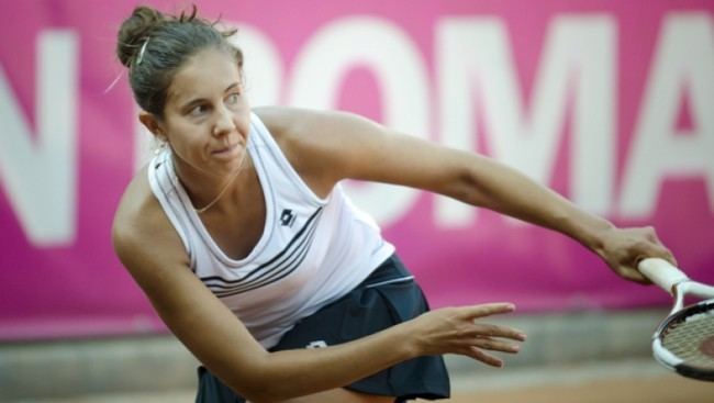 Mihaela Buzarnescu wearing a white top, and a black skirt while playing tennis.