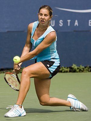 Mihaela Buzarnescu wearing a necklace, a blue top, a black, and blue shorts while playing tennis.