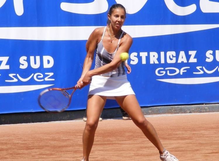 Mihaela Buzarnescu wearing a sexy top, a white skirt, and white shoes while playing tennis.