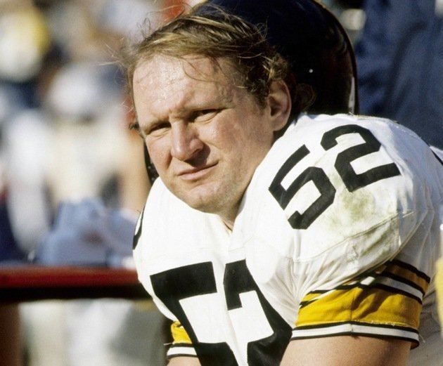 Mike Webster with a furrowed brow while wearing a white, black, and yellow football jersey with number fifty-two
