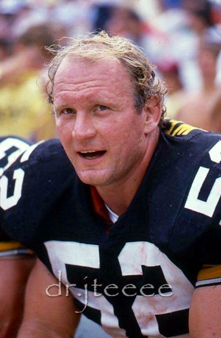 Mike Webster with a furrowed forehead and his mouth is open while wearing a black, white, and yellow football jersey with number fifty-two