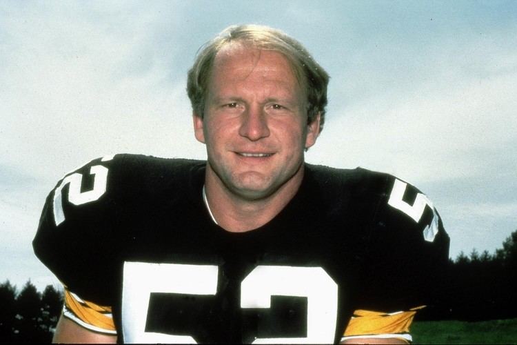 Mike Webster smiling while wearing a black, white, and yellow football jersey with number fifty-two