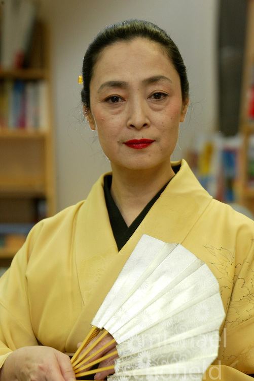 Mineko Iwasaki wearing yellow kimono while holding white hand fan