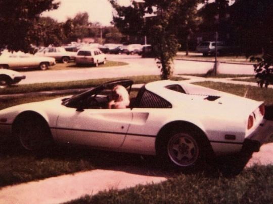 Miranda Grosvenor riding on a white Ferrari with her blonde hair and a few other cars in her background in an old photograph