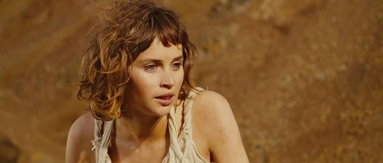 Felicity Jones as Miranda, talking to someone with a serious face and shoulder-length messy hair in a scene from the 2010 American fantasy comedy-drama film, The Tempest. She is wearing a white sleeveless dress.