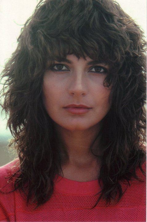 Mirella D'Angelo with a serious face and black wavy hair while wearing a red net blouse