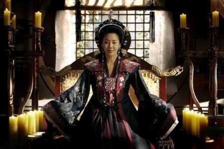 Go Hyun-jung as Lady Mishil smiling while sitting on the throne in a scene from the 2009 historical drama Queen Seondeok