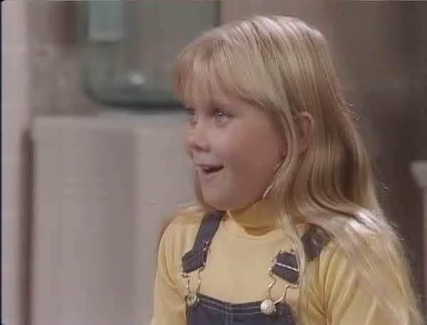 Missy Gold as Katey Gatling wearing a yellow shirt under a blue jumper in a...