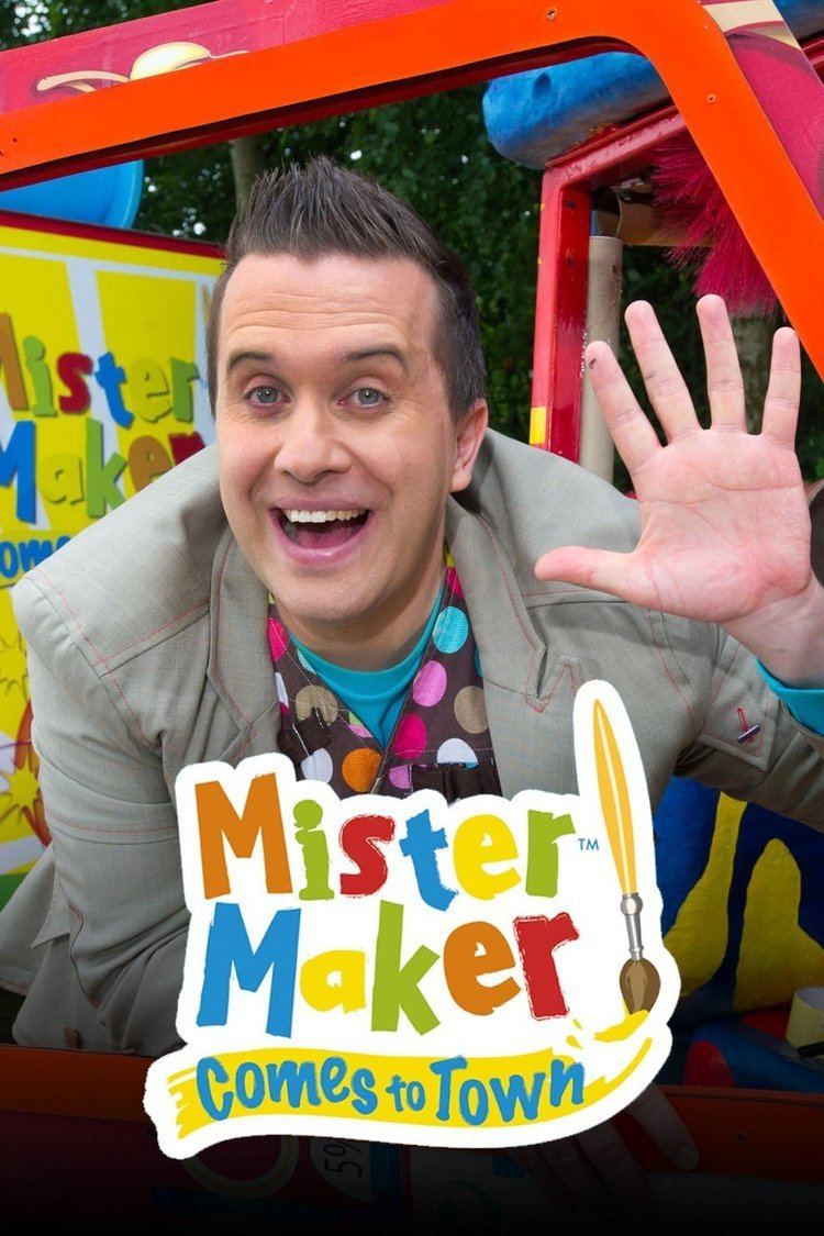 Phil Gallagher with a big smile while waving his hand, wearing a khaki coat over a polka dot printed shirt in Mister Maker Comes to Town,  a spin-off of children's television series.