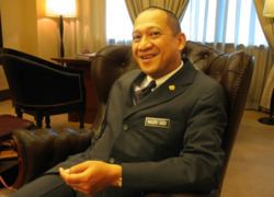 Mohamed Nazri Abdul Aziz smiling while inside an office wearing a coat with a badge on the side.