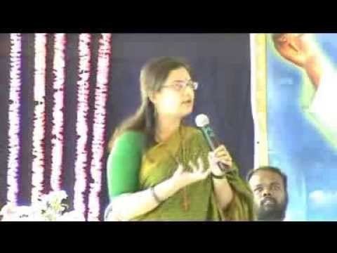 Mohini wearing eyeglasses, and green traditional Indian clothing for women while holding a microphone.