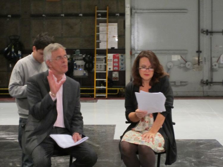 Moira Brooker and Philip Bretherton both wearing eyeglasses and reading scripts.