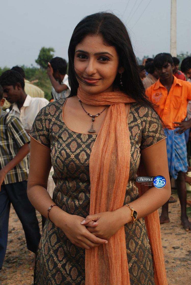 Monica smiling while wearing an orange scarf, black and orange dress, necklace, bracelet, and wristwatch