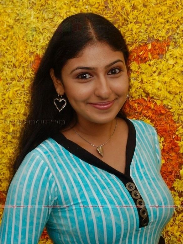 Monica smiling while wearing a white and blue striped blouse, heart necklace, and heart earrings