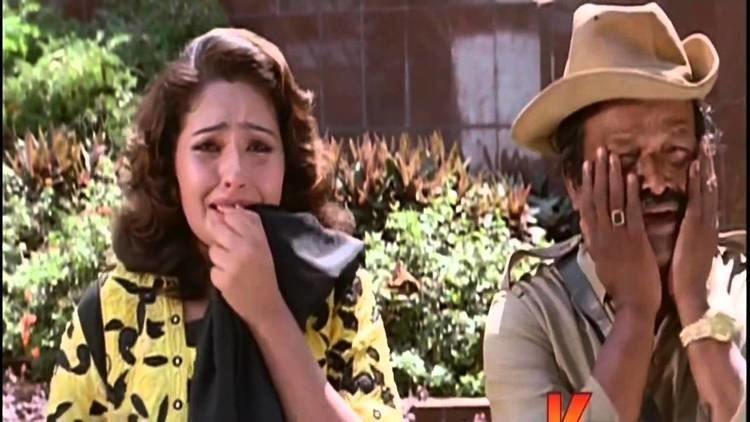 Mumtaj as Monisha crying and wearing a black and yellow dress, and a black scarf with a man holding his face and wearing a hat in a movie scene from Monisha En Monalisa (1999 film).