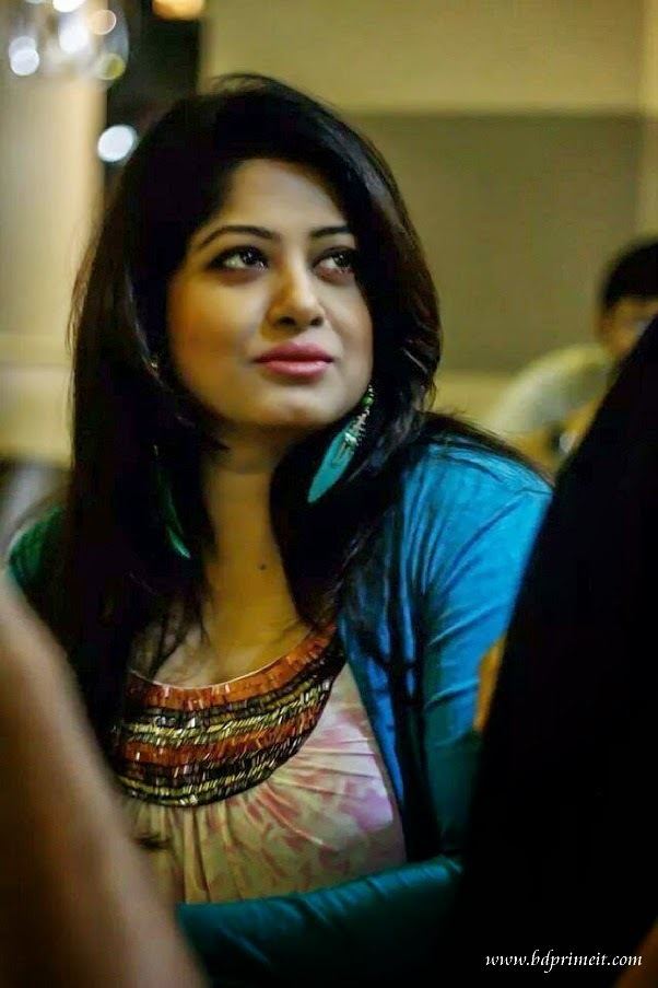 Moushumi looking afar while wearing a blue blazer, blue earrings, and pink blouse with black and orange sequins