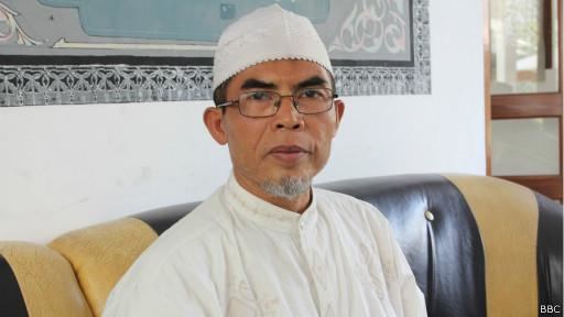 Muhammad Sholeh Ibrahim sitting on the couch while wearing a white taqiyah, eyeglasses, and white long sleeves