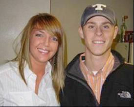 Channon Christian and Christopher Newsom are smiling while Channon with blonde straight hair is wearing a white blouse and Christopher is wearing a gray cap and white shirt under an orange polo and black jacket