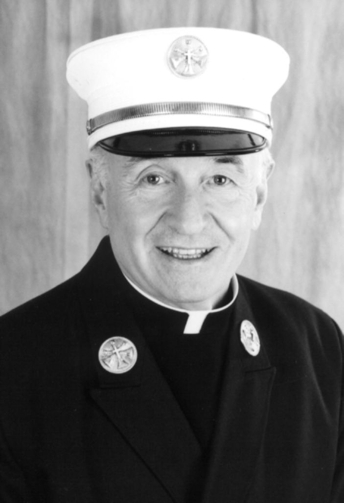 Mychal Judge smiling while wearing a peaked cap, a coat with badges, and long sleeves