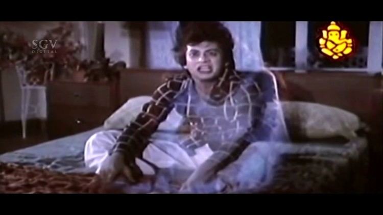 Anant Nag as Krishna with a frightened face while sitting on a bed and wearing brown checkered long sleeves and white pants in a movie scene from Naa Ninna Bidalaare, a 1979 Indian Kannada-language horror film.