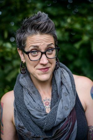 Nadia Bolz-Weber posing while having a standing hairstyle and wearing a sleeveless shirt and a thick gray scarf.