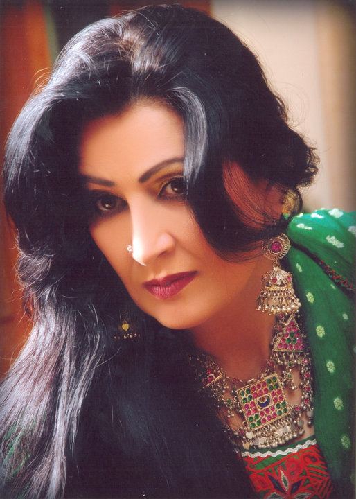 Naghma with a strict face looking at something with her hair down, a nose piercing, a silver necklace, and danglings earrings wearing a green salwar kurta
