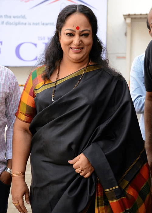 Nalini smiling while wearing a black and checkered dress paired with some pieces of jewelry