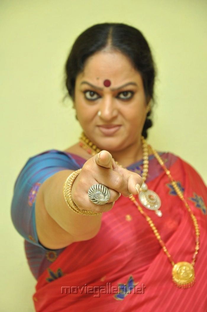 Nalini pointing her finger with an angry facial expression while wearing a blue and red dress paired with some pieces of gold jewelry