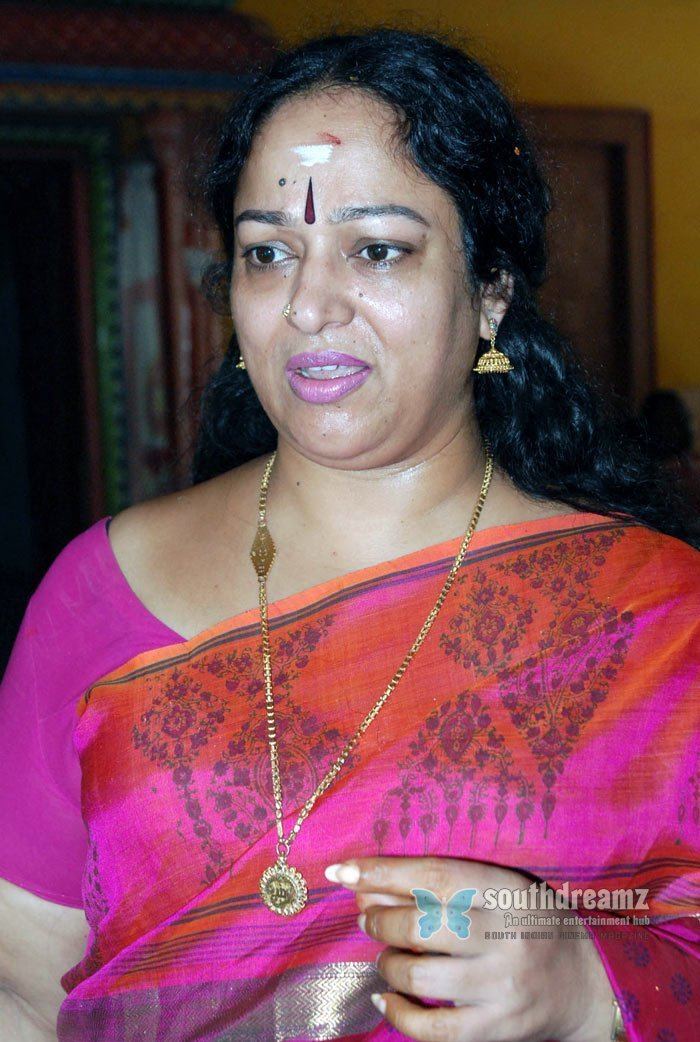 Nalini looking at something while wearing a purple and orange dress, gold earrings, and a gold necklace