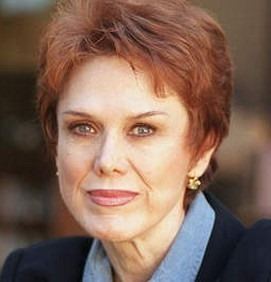 Nancy Dow smiling closed mouth with reddish hair and wearing a blue coat over a sky blue dress.