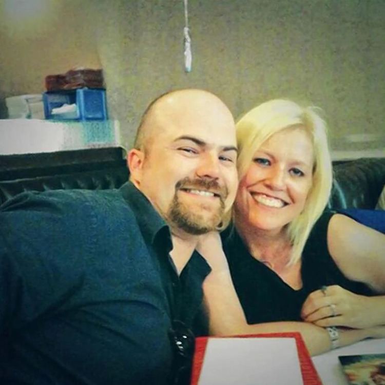 Nancy Motes and John Dilbeck are smiling. Nancy with blonde hair and wearing a black sleeveless shirt while John wearing a black polo shirt.