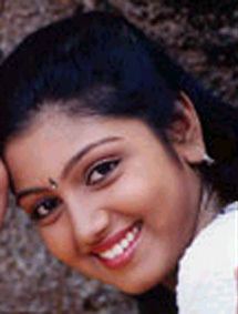 Nandana smiling, with black hair, wearing earrings, and a white top.