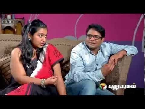 Nandana is talking while Manoj Bharathiraja is looking at her while sitting on a brown sofa during an interview. Nandana with a serious face, long wavy hair, wearing earrings, and a red, white, and black Indian dress while Manoj wearing eyeglasses, light blue long sleeves, and blue jeans.